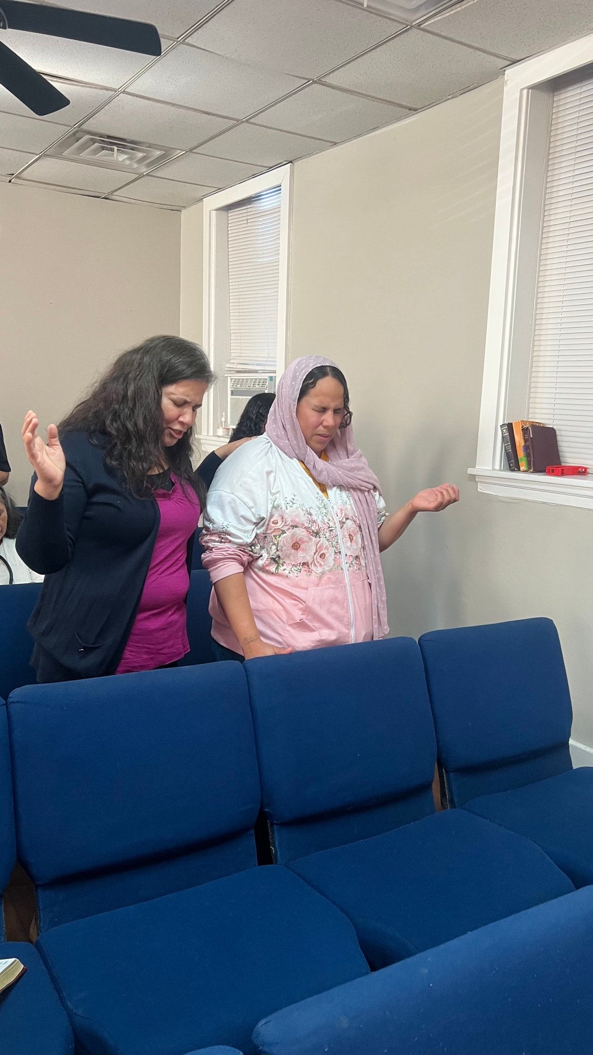 Dos hermanas orando con las manos levantadas durante el servicio